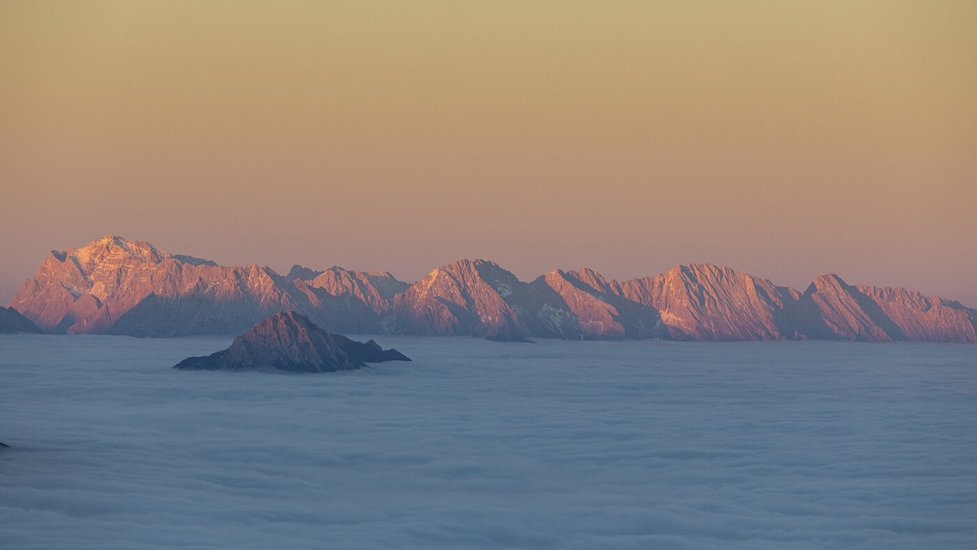 Berggipfel ragen bei Sonnenaufgang über ein Nebelmeer in den Alpen.