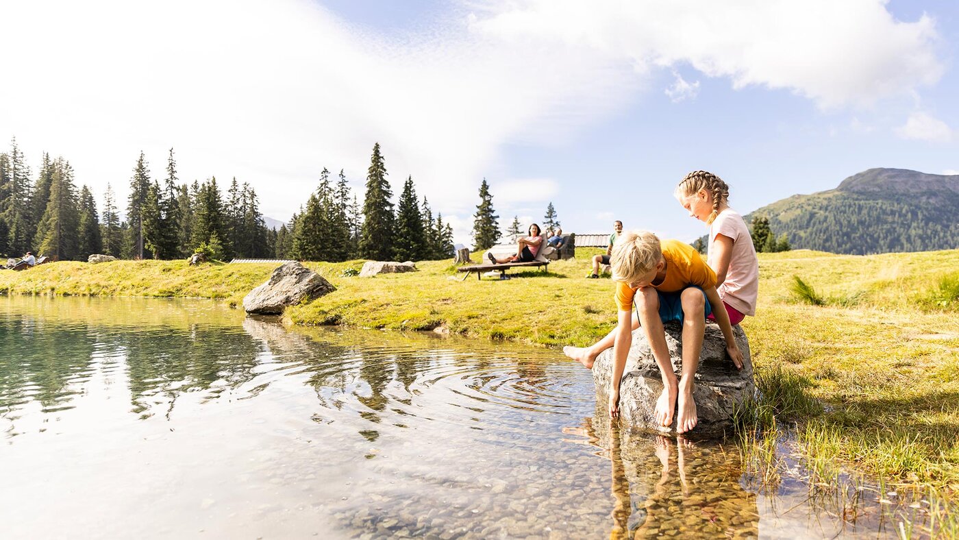 Kinder sitzen am Ufer des Högsees und spielen im klaren Wasser.