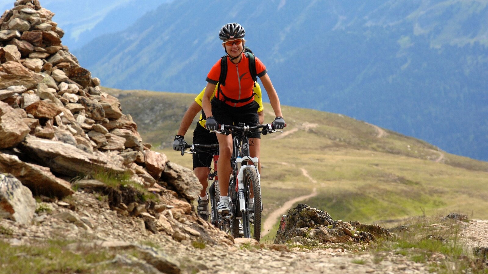 Zwei Mountainbiker auf felsigem Höhenweg, weite Berglandschaft – Aktivurlaub in Serfaus im Apart Rubin.